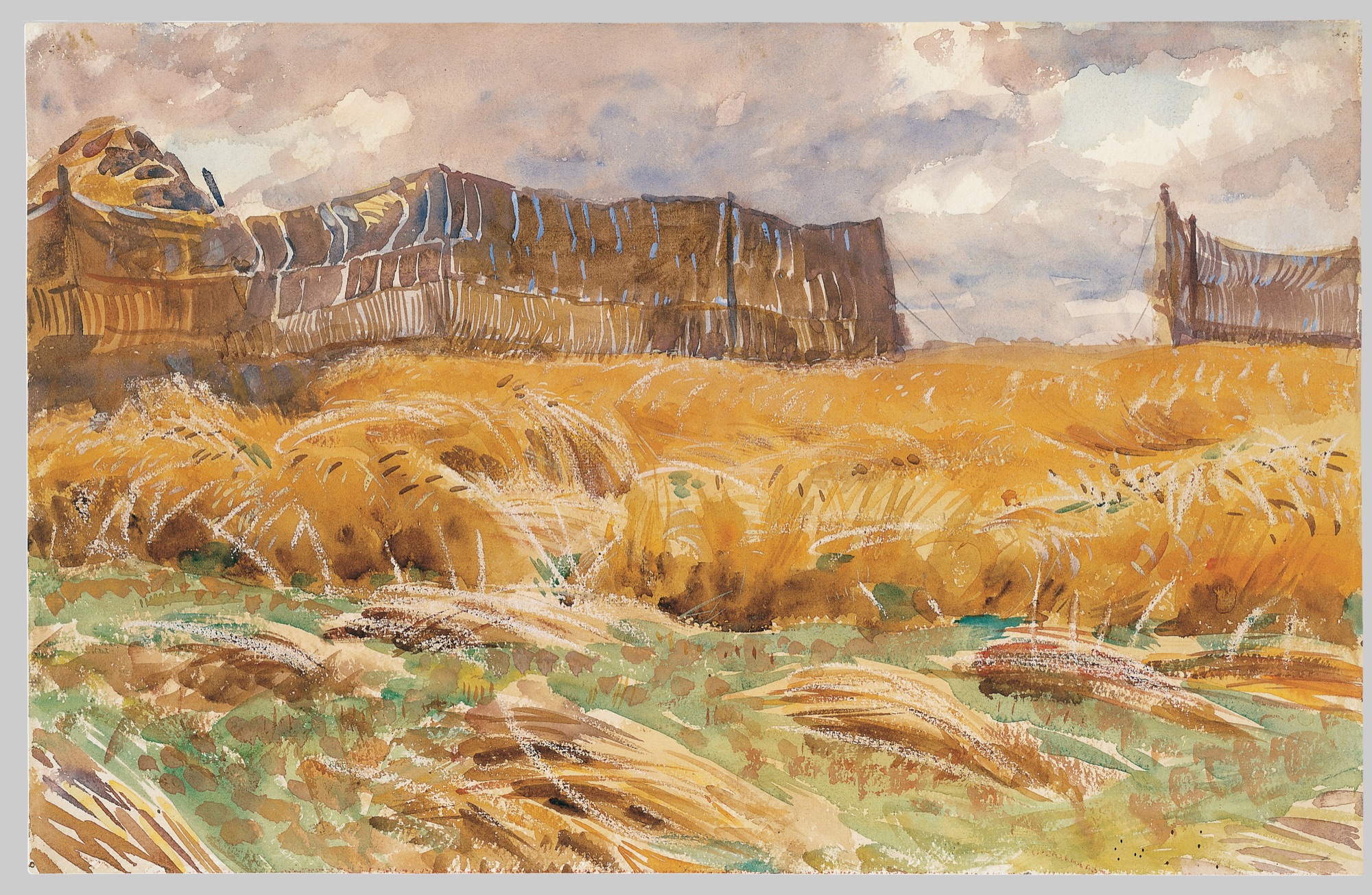 A wheat field in full harvest gold leans in the wind below weathered brown windbreak fences, under a sky of moving mauve-gray clouds